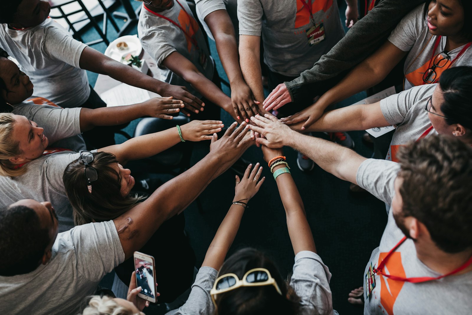 Seen from above, a dozen hands from a dozen people meet and overlap in the centre of a circle.