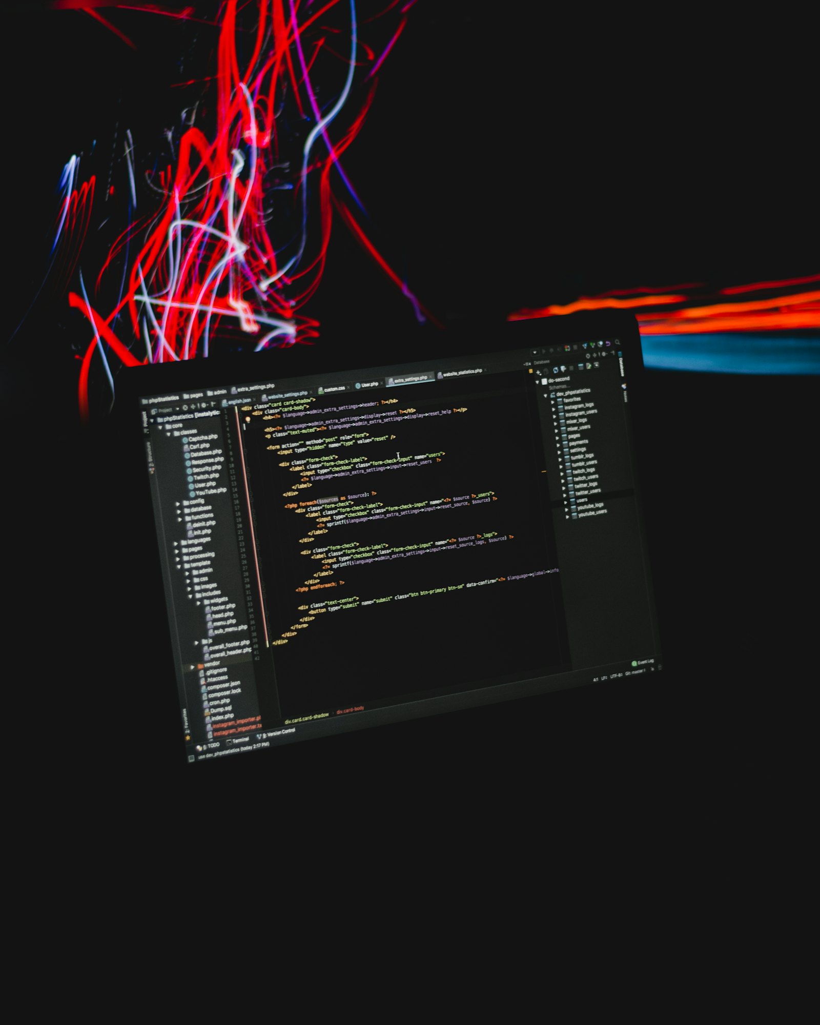 A laptop in a darkened room showing a dense screen of source code, streaked by red and blue light trails.